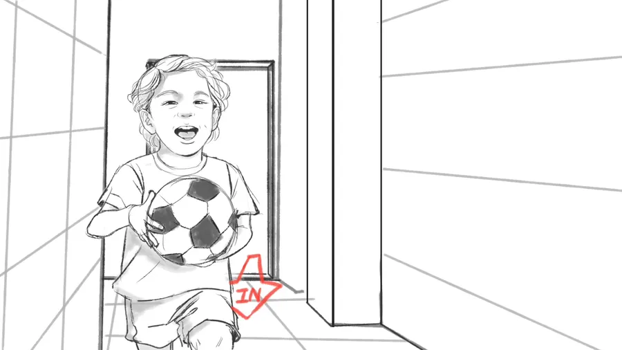 A toddler sits on a floor beside a football, laughing.