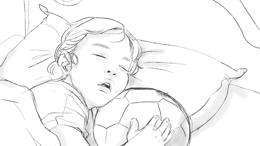 A child asleep on a bed with an arm over a football.